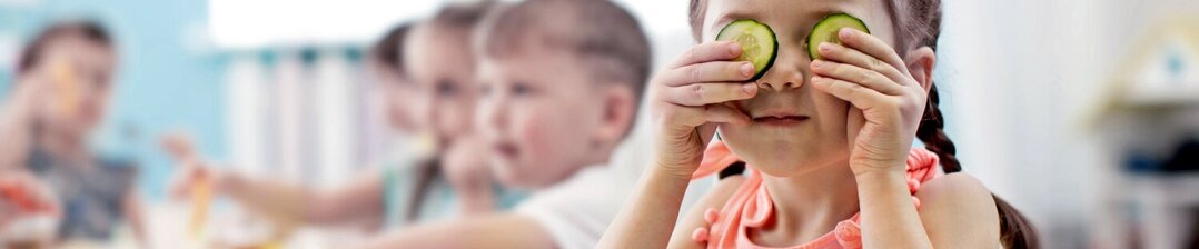 Óvodás kislány játékosan uborkát tart az arcába